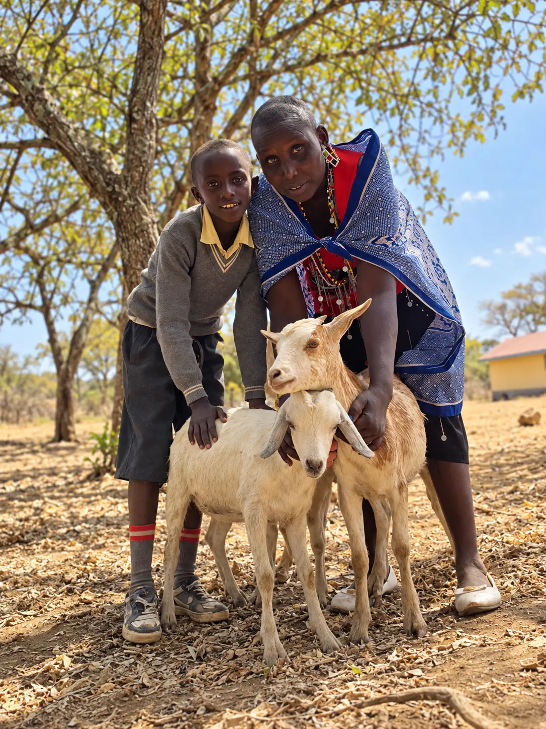 Lillian standing with a student and their pair of goats outside their home in rural Kenya