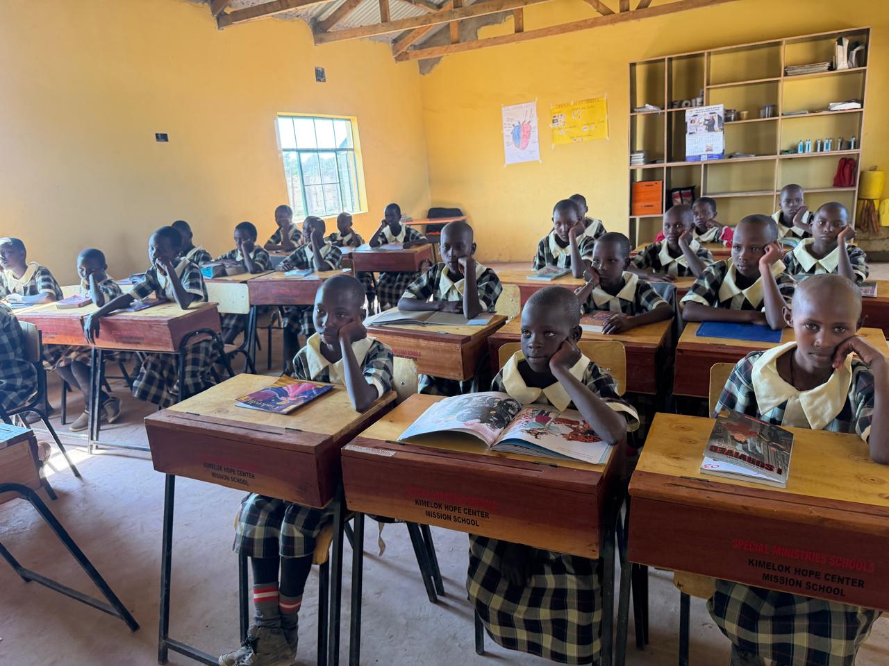 Girls in uniform seated at wooden desks in a rural Kenyan classroom, ready to learn