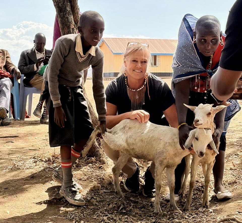 A Kenyan family and a visitor presenting a pair of goats to a family outside their home