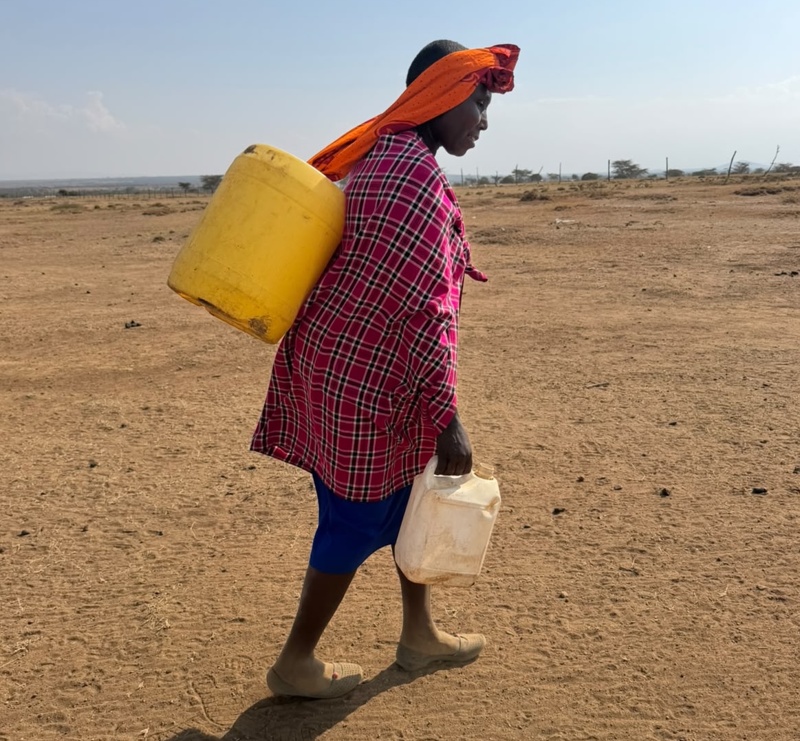 Kenyan woman walking across dry land carrying water containers